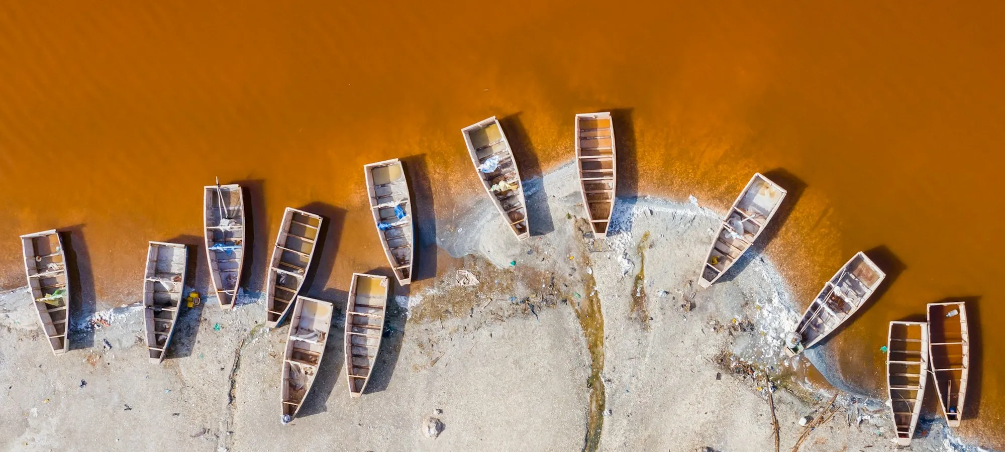 Vue aérienne d'une rangée de pirogues alignées sur la rive d'un lac ocre