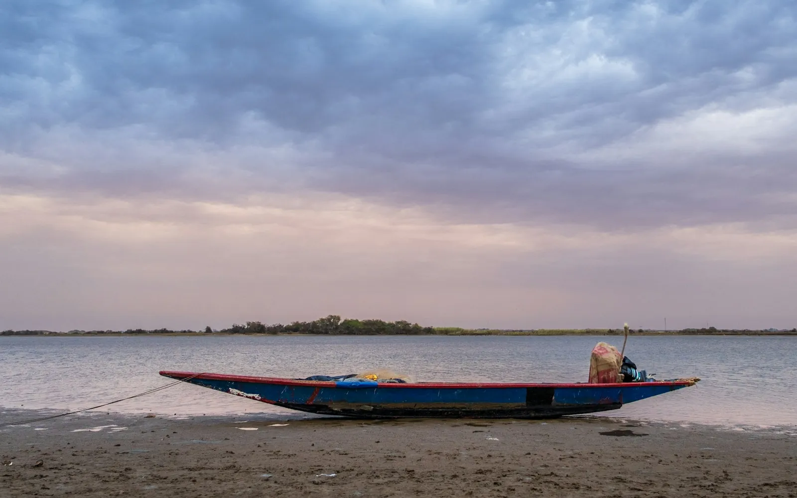 Une pirogue échouée sur une rive plate, sous un ciel couvert au petit matin